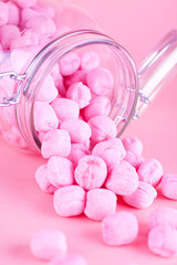 Glass jar filled with pink candy. Studio photo isolated on pink background. Selective focus on object.
