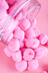Glass jar filled with pink candy. Studio photo isolated on pink background. Selective focus on object.