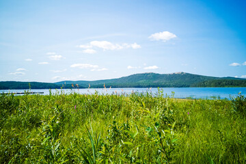 Fototapeta na wymiar Lake landscape. The view on a green mountains on a sunny summer day. Schoenopluctus lacustris.