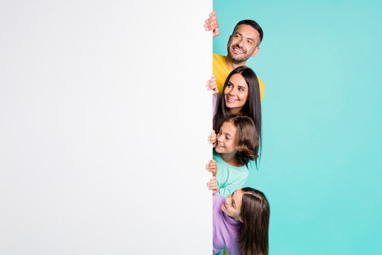 Photo portrait of big family hiding behind big white placard poster with small children isolated on vivid teal colored background
