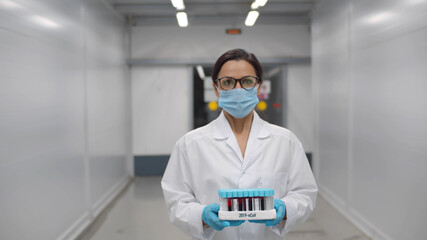 Woman doctor in safety mask and gloves carrying tray with blood samples for covid-19 test