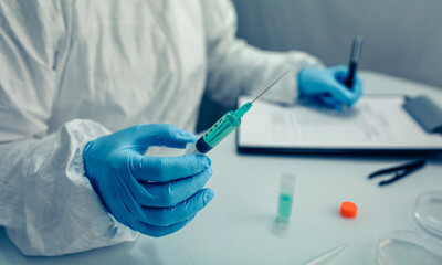 Scientist hand holding a syringe with virus vaccine in the laboratory. Selective focus on vaccine in the foreground