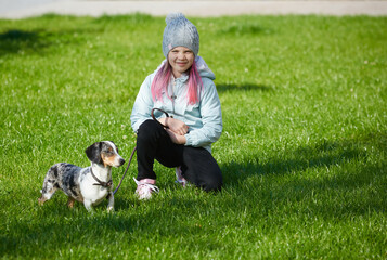 Girl child playing with dachshund dog in autumn sunny park