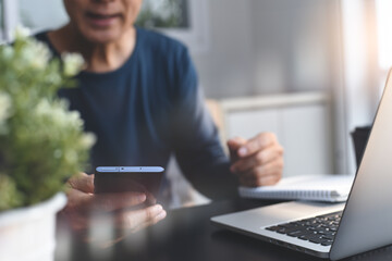 Man video calling via mobile phone during working on laptop computer from home office