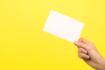 Female hand holding a white card on a yellow background