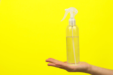 Antiseptic bottle on a female hand on a yellow background