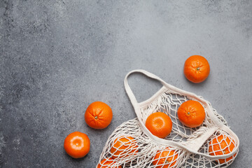 Tangerines in an eco-friendly string bag on a grey background in a flat lay with selective focus.