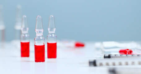 Red glass ampoule with medicine or vaccine against measles, rubella, flu or coronavirus on a blue background with a copy space
