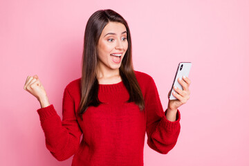 Photo of cute young girl hold smartphone raise fist open mouth wear red sweater isolated pink color background