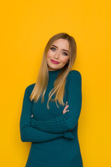 Fototapeta premium Beautiful Young Woman In Teal Fitted Dress Is Posing With Arms Crossed
