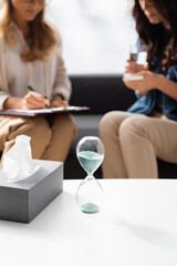 blurred view of doctor and patient and hourglass, tissues on foreground, stock image