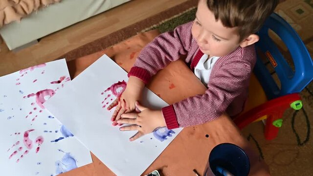 Top view of colored handprints on a sheet of paper. Boy draws color paints. Developing activities at home.