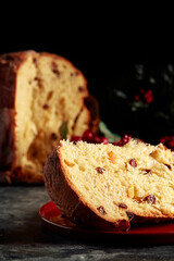 Portion of christmas panettone on a red plate. In the background the Christmas Easter bread and mistletoe. Dark background