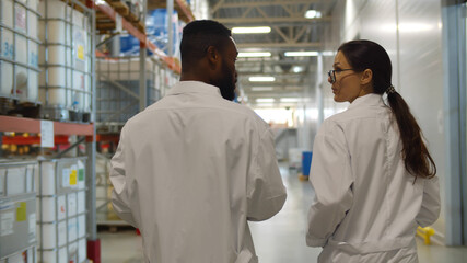 Back view of african and caucasian engineers in lab coats examining industrial warehouse