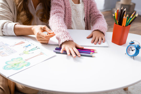 cropped view of girl drawing pictures with colorful pencils while visiting psychologist