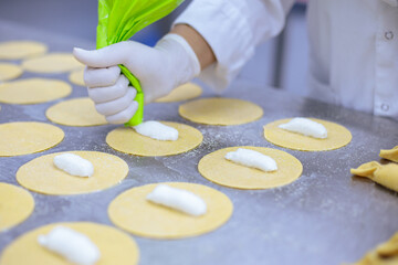 Woman’s hands, with nylon gloves on, using a pastry bag to squeeze a cheese stuffing onto pasta...