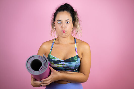 Young beautiful woman wearing sportswear and holding a splinter over isolated pink background making fish face with lips, crazy and comical gesture.