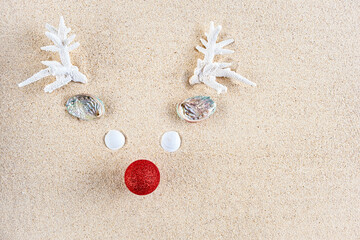 Reindeer made from she shells and white corrals with red Christmas ball as a nose, on clean tropical sand, top view