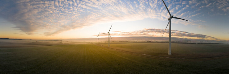 Aerial view of three wind turbines in the early morning fog at sunrise in the English countryside panorami