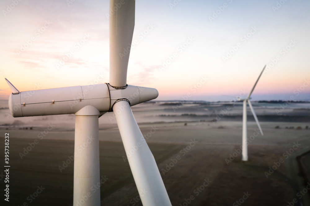 Wall mural aerial view of two wind turbines close up at sunrise in the fog in the english countryside