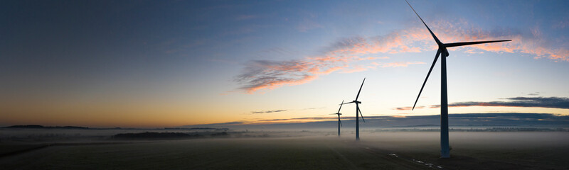 Aerial view of three wind turbines in the early morning fog at sunrise in the English countryside...
