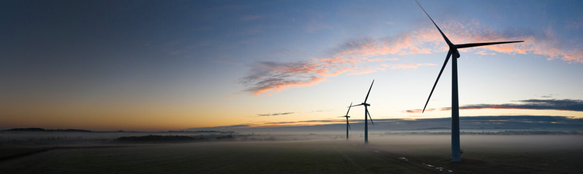 Aerial View Of Three Wind Turbines In The Early Morning Fog At Sunrise In The English Countryside Panoramic