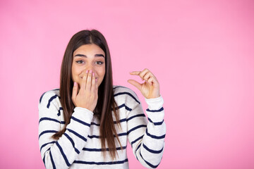 Beautiful young woman holding something very tiny, size concept. It is so small. Studio portrait of pretty young woman showing small size with her fingers. Pink  background.