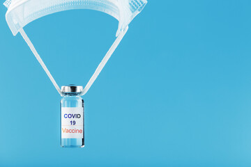 Ampoules with a vaccine against the coronavirus infection COVID-19 were dropped by parachute from a protective mask on a blue background.