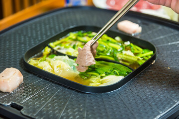 Chopstick holding raw wagyu beef in boiling soup.Shabu Shabu or Sukiyaki or hot pot ,Hand holding pork using chopsticks