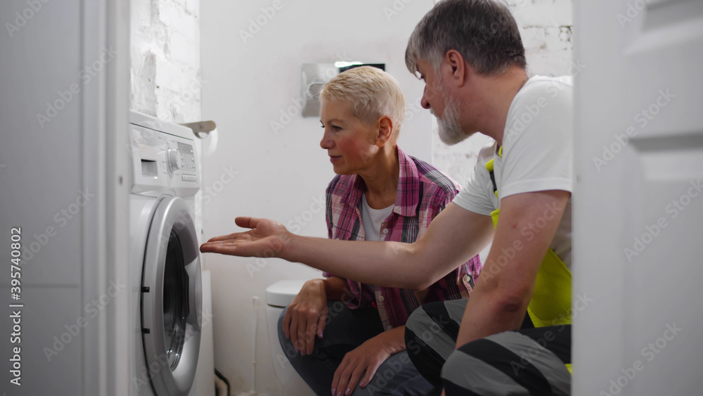 Wall mural Senior repairman fixing washing machine for woman client