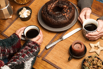 Manos de mujer y hombre junto a dos tazas de café con un bizcocho de chocolate sobre una mesa...