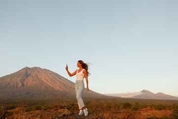 A woman looks at a mountain, a volcano and taking picture on the phone. Rear view. Bali. Agung.