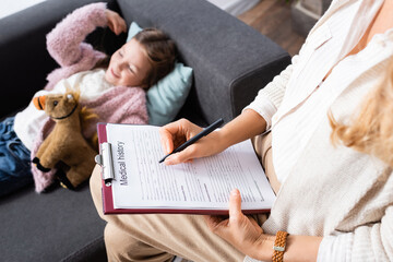 cropped view of psychologist writing in medical history while little girl telling story, stock image