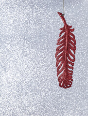 Red feather on a bright, glare background. Christmas decoration for a tree or home. Festive mood.