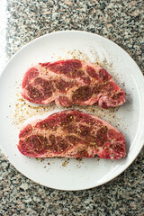 Fresh raw seasoned pork steak meat slices set on white porcelain dish on kitchen table