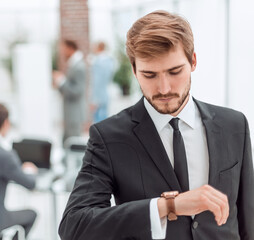 Fototapeta premium serious businessman standing in the office and looking at his wrist watch