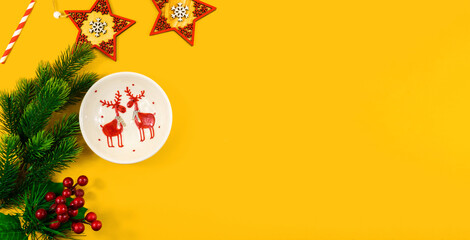 Christmas composition, plate with a deer, fir branches, berries and decorations, yellow background banner, copy space
