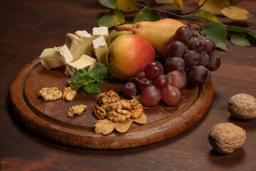 Appetizer plate of fruits, grapes, nuts on a dark wooden plate and wooden table. Wine snacks set: selection of cheese, grapes, pear and walnuts on a wooden board.