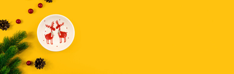 Christmas composition, plate deer, pine cones and fir branches, yellow background with copy space, flat lay, banner