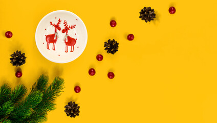 Obraz na płótnie Canvas Christmas composition, decorative tableware, cones, berries, fir branches, yellow background with copy space, banner