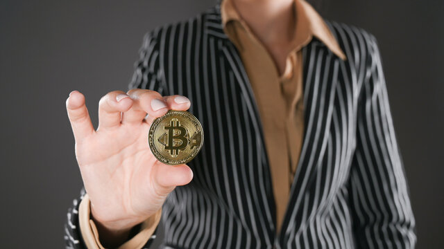 Woman in a suit holds a bitcoin in her hand