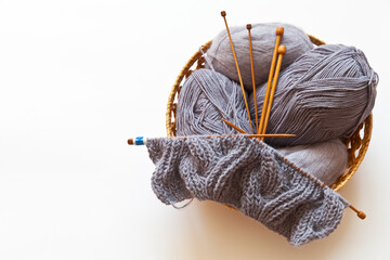 Basket with needlework on a white background. Balls of gray woolen and mohair yarn, wooden knitting...