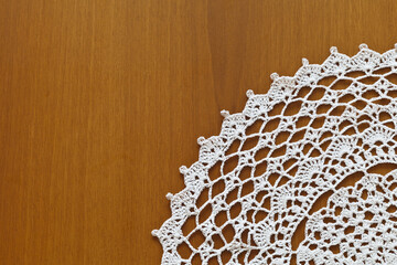 Fragment of a lace napkin from natural cotton yarn, crocheted by hand on a wooden table. Crochet as...