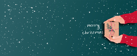Female's hands in pullover holding Christmas gift box decorated with evergreen branch on red background with snow. Christmas and New Year banner.