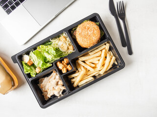 Lunch box in black plastic package for take away or food delivery and laptop