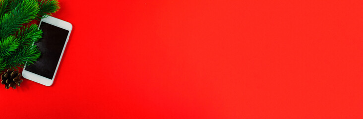 Winter christmas composition, phone, fir branches and cones, red background, copy space, flat lay, wide banner