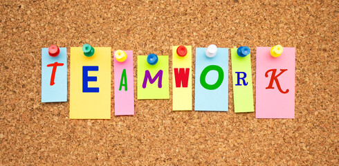 Multicolor notes with letters pinned on a cork board. Word TEAMWORK.
