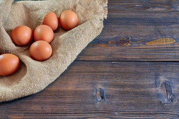 Chicken eggs on a burlap napkin on a dark wooden background