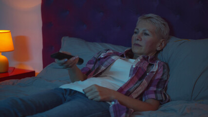 Senior woman lying on bed and changing channels on tv