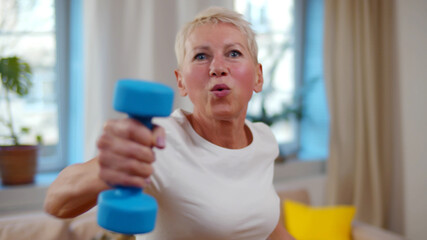 Senior woman doing exercises with dumbbells in living room